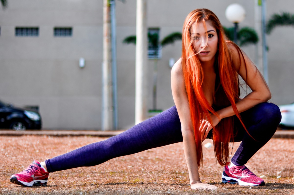 Viviane Lua em alongamento ao ar livre, legging roxa, cabelo ruivo solto, cenário urbano