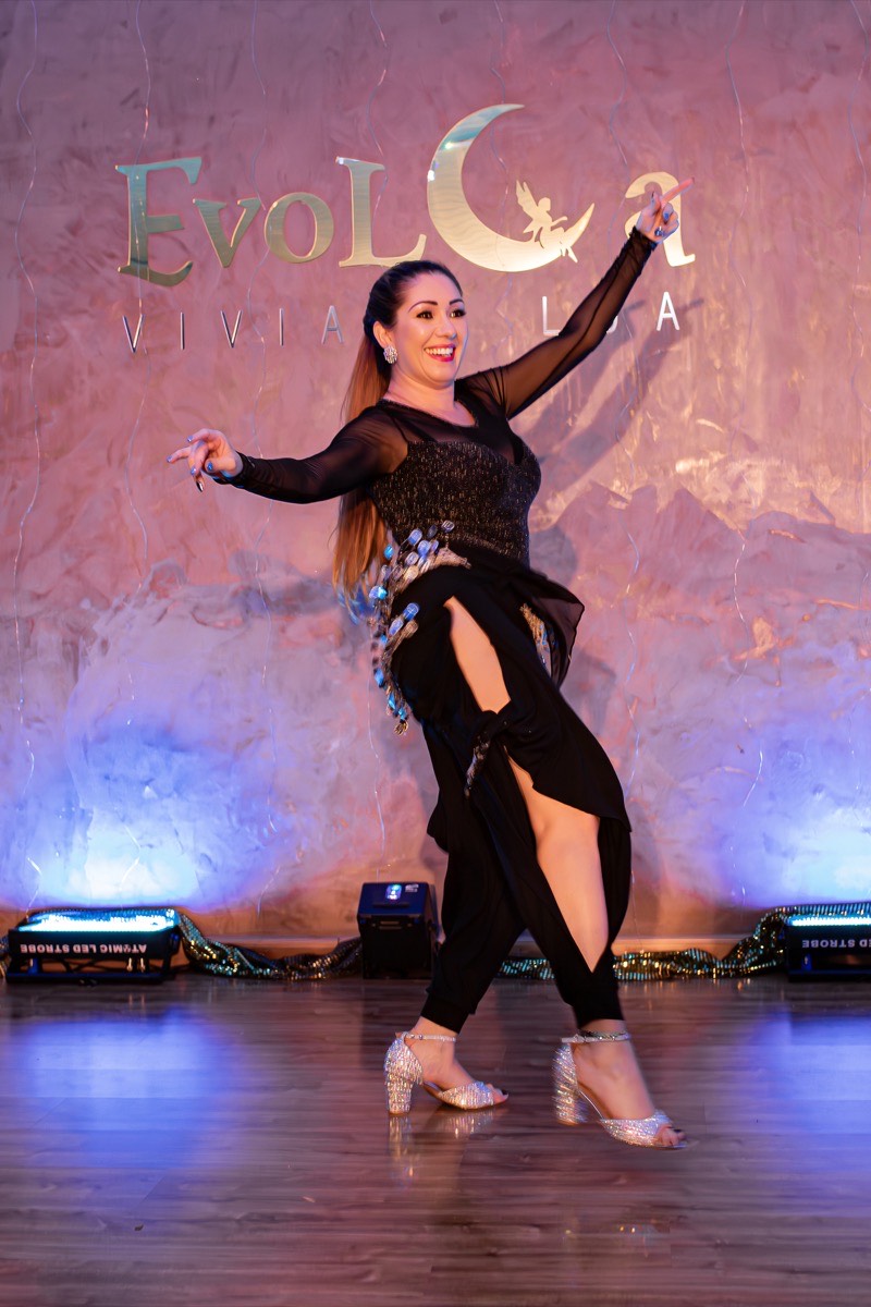 Viviane Lua solo no palco, figurino preto com fenda, backdrop EvoLua, pose de dança