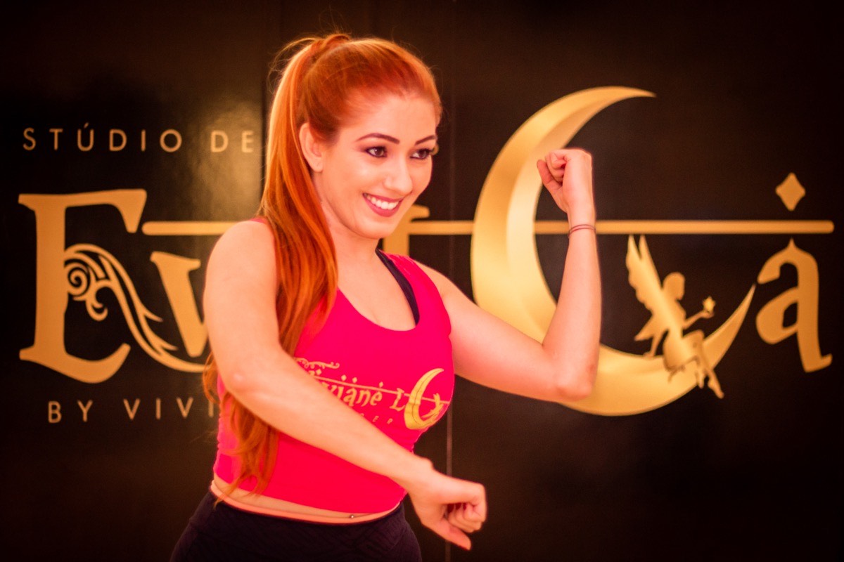 Viviane Lua em pose flexionando o braço, top pink, backdrop Stúdio EvoLua